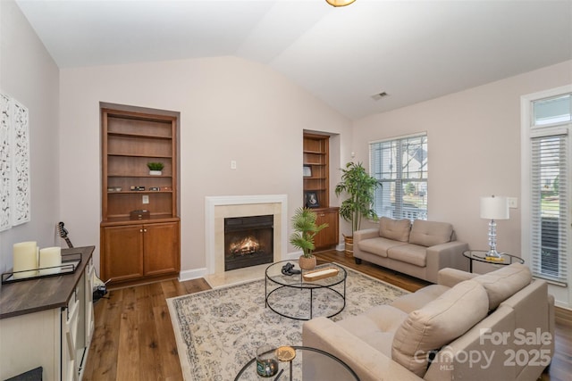 living room with visible vents, built in shelves, wood finished floors, a high end fireplace, and lofted ceiling