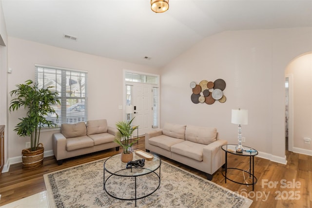 living area featuring visible vents, baseboards, lofted ceiling, wood finished floors, and arched walkways