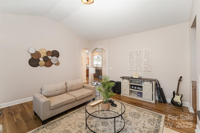 living room featuring lofted ceiling, wood finished floors, arched walkways, and baseboards