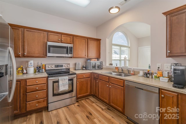kitchen with a sink, stainless steel appliances, arched walkways, and brown cabinets