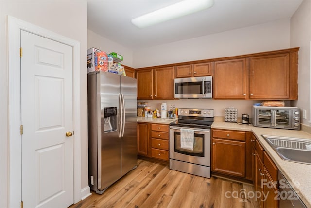 kitchen with a sink, stainless steel appliances, light wood-style floors, brown cabinetry, and light countertops