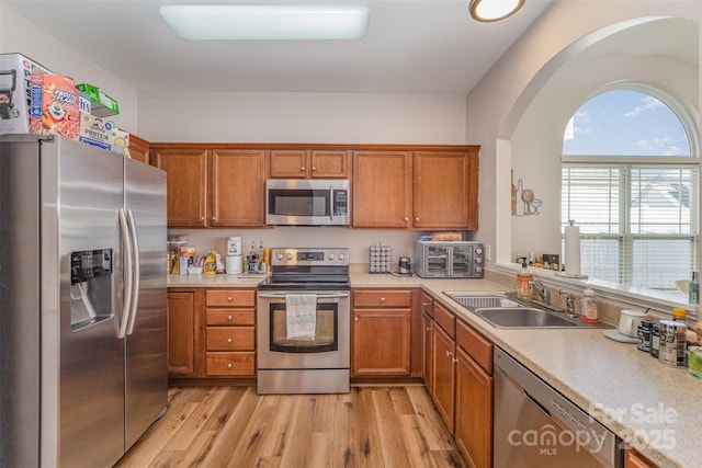 kitchen featuring light countertops, appliances with stainless steel finishes, light wood-style floors, brown cabinetry, and a sink