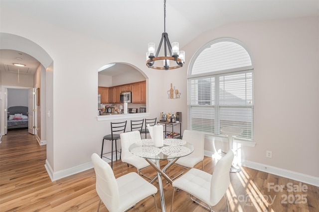 dining space with light wood finished floors, baseboards, attic access, a chandelier, and vaulted ceiling