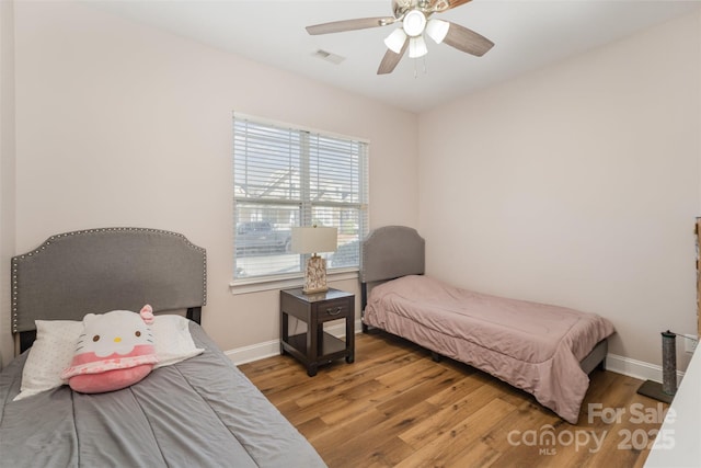 bedroom featuring visible vents, a ceiling fan, baseboards, and wood finished floors