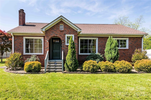 view of front of home featuring fence, a shingled roof, brick siding, and a front yard