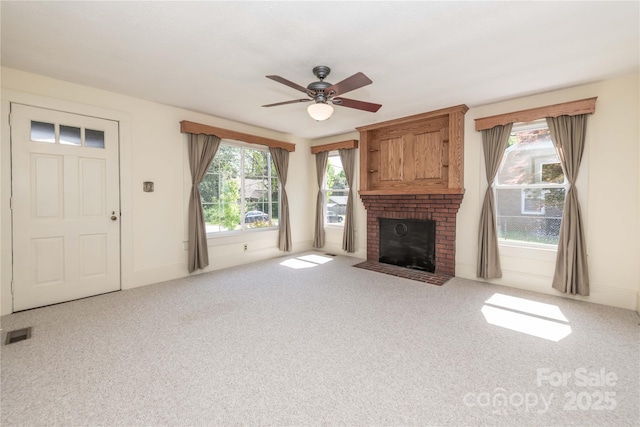 unfurnished living room with a fireplace, carpet floors, visible vents, and a ceiling fan