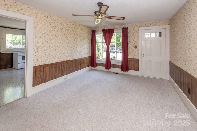 interior space featuring wainscoting, wood walls, a ceiling fan, and wallpapered walls