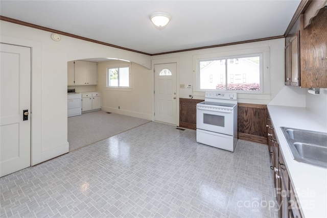 kitchen with white electric stove, a sink, arched walkways, washing machine and clothes dryer, and baseboards