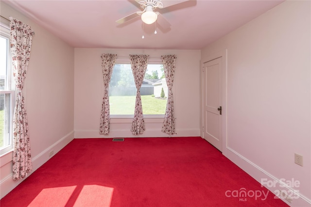 unfurnished room featuring dark colored carpet, visible vents, a ceiling fan, and baseboards