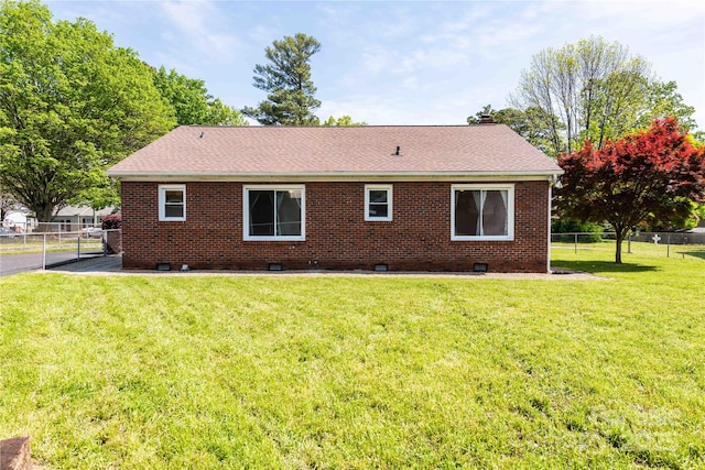 rear view of house featuring roof with shingles, fence, brick siding, a yard, and crawl space