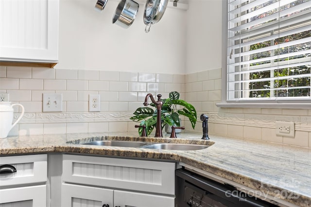kitchen with white cabinets, light stone countertops, backsplash, and a sink