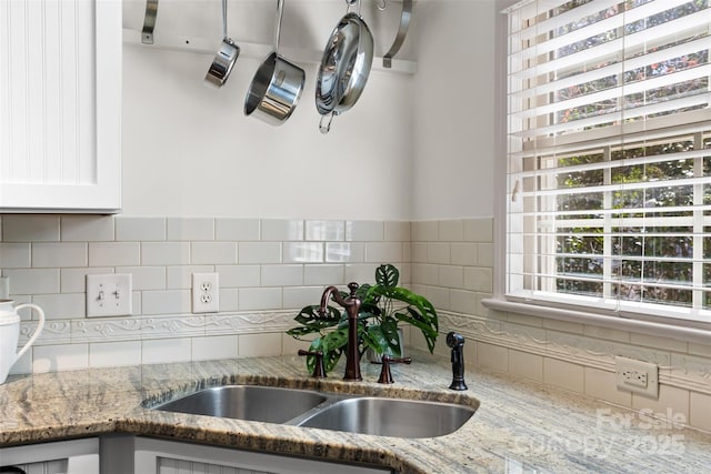 details with light stone counters, decorative backsplash, white cabinets, and a sink