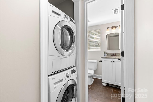 washroom with tile patterned floors, visible vents, a sink, stacked washer / drying machine, and laundry area