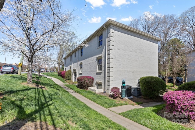 view of home's exterior with cooling unit, a lawn, and brick siding