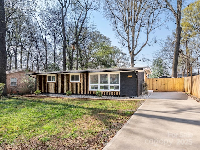 view of front of house with board and batten siding, a front yard, driveway, and fence