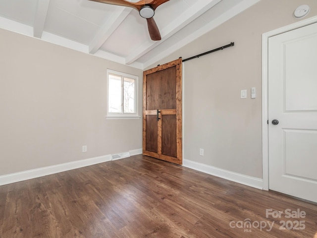 unfurnished bedroom with visible vents, baseboards, a barn door, dark wood-style floors, and vaulted ceiling with beams