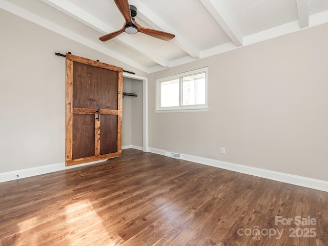 empty room featuring baseboards, dark wood-style floors, a barn door, ceiling fan, and vaulted ceiling with beams