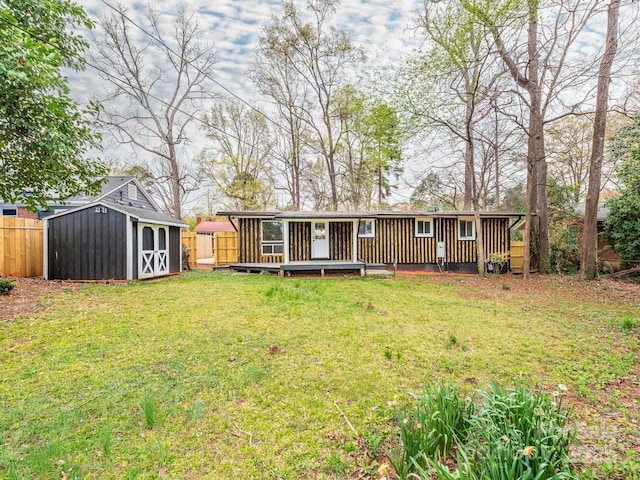 rear view of property featuring a lawn, a shed, an outdoor structure, and fence
