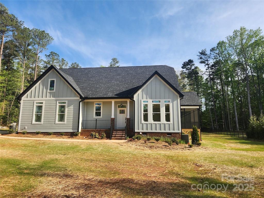 view of front of home featuring a shingled roof, covered porch, board and batten siding, and a front lawn