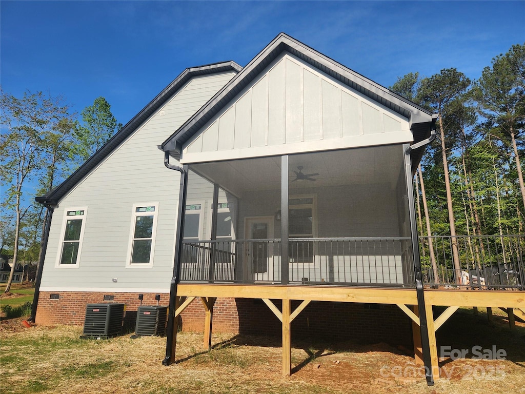 back of house with board and batten siding, crawl space, a ceiling fan, a sunroom, and central AC