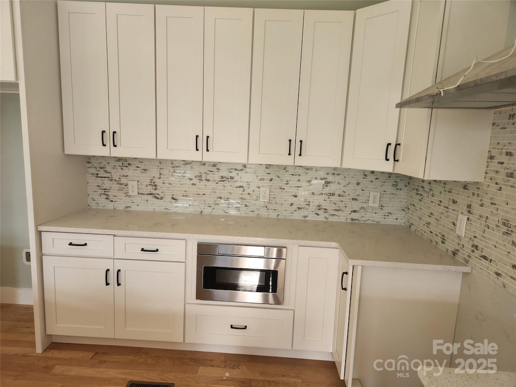 kitchen with light countertops, decorative backsplash, under cabinet range hood, and white cabinetry