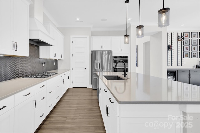 kitchen with a sink, custom exhaust hood, a center island with sink, stainless steel appliances, and ornamental molding