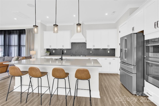 kitchen with decorative backsplash, a sink, custom exhaust hood, light wood finished floors, and stainless steel appliances