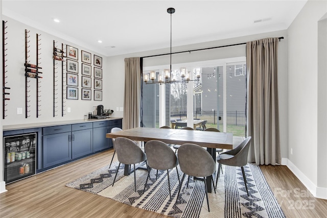 dining space with an inviting chandelier, light wood finished floors, baseboards, wine cooler, and visible vents