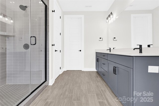 full bath featuring double vanity, baseboards, wood tiled floor, a shower stall, and a sink