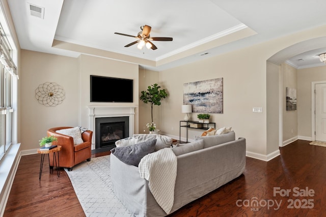 living area with visible vents, wood finished floors, a ceiling fan, arched walkways, and a tray ceiling