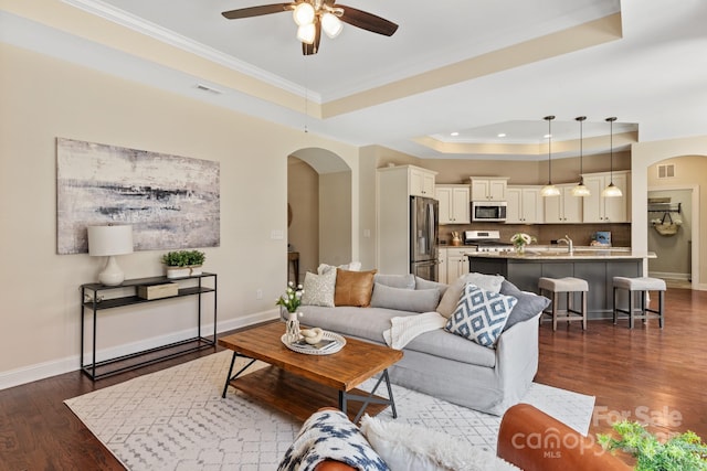 living room with a ceiling fan, arched walkways, a tray ceiling, and visible vents
