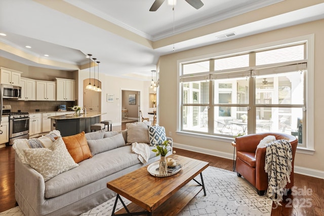 living area with a ceiling fan, ornamental molding, a tray ceiling, and visible vents
