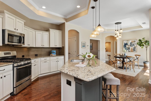 kitchen featuring a sink, arched walkways, appliances with stainless steel finishes, and a raised ceiling
