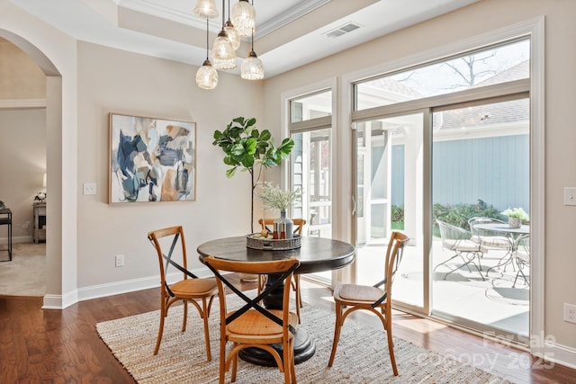 dining space with baseboards, wood finished floors, arched walkways, and a raised ceiling