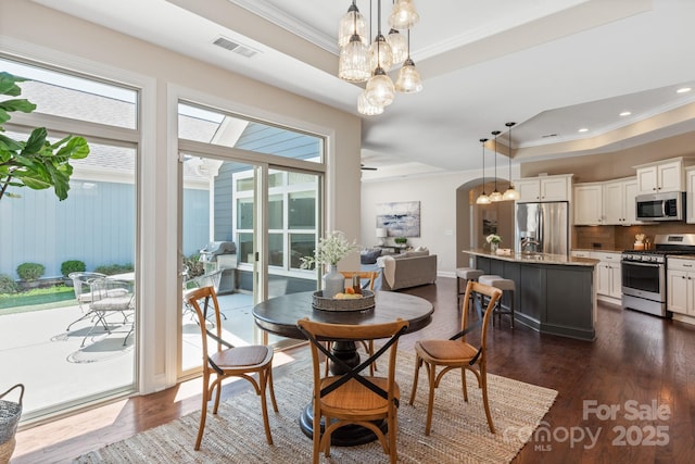 dining room featuring a tray ceiling, ornamental molding, a chandelier, dark wood-style floors, and visible vents
