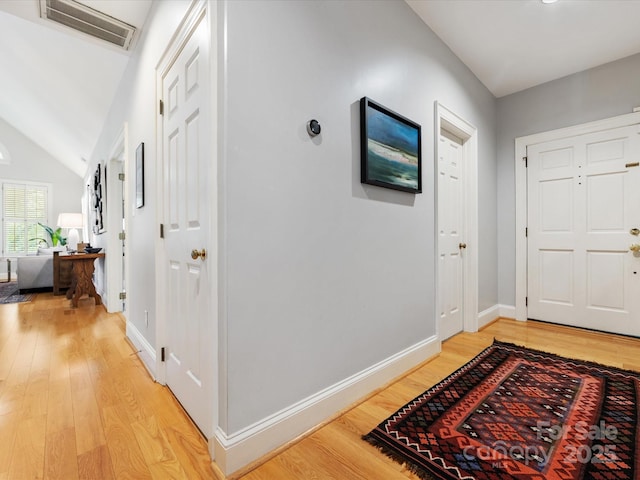 hall featuring baseboards, visible vents, light wood-style floors, and vaulted ceiling