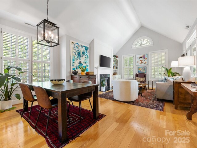 dining area featuring a premium fireplace, an inviting chandelier, high vaulted ceiling, visible vents, and light wood-style flooring