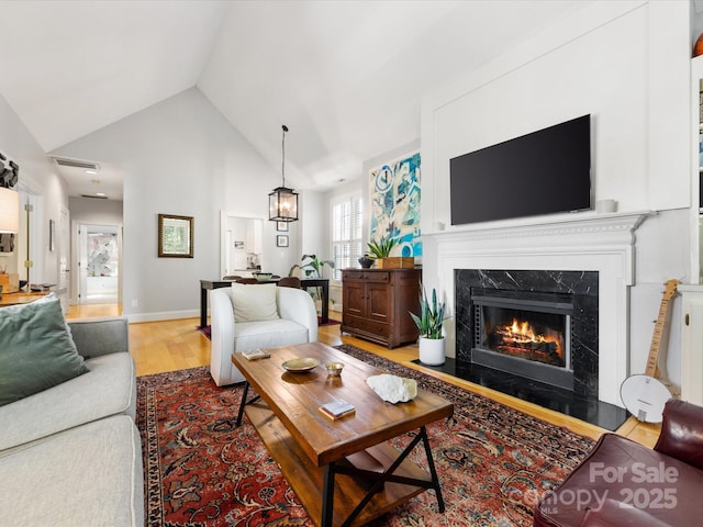 living room featuring a fireplace, high vaulted ceiling, baseboards, and light wood finished floors