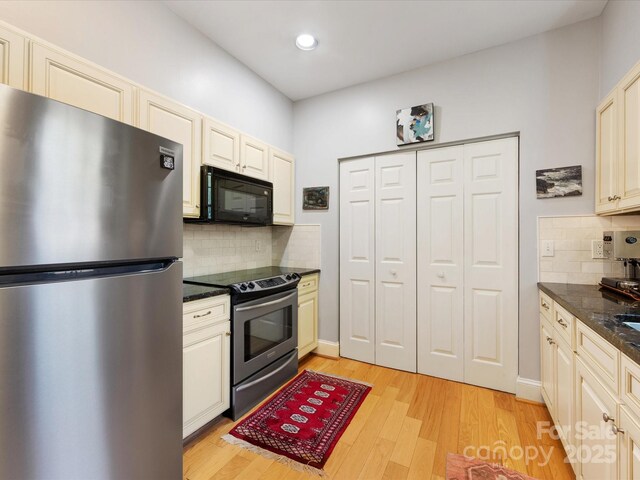 kitchen featuring tasteful backsplash, light wood-type flooring, dark stone counters, cream cabinetry, and appliances with stainless steel finishes