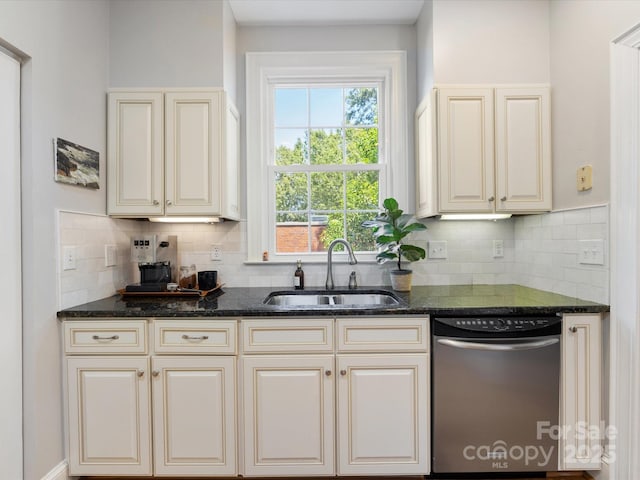 kitchen with stainless steel dishwasher, cream cabinetry, a sink, and dark stone counters