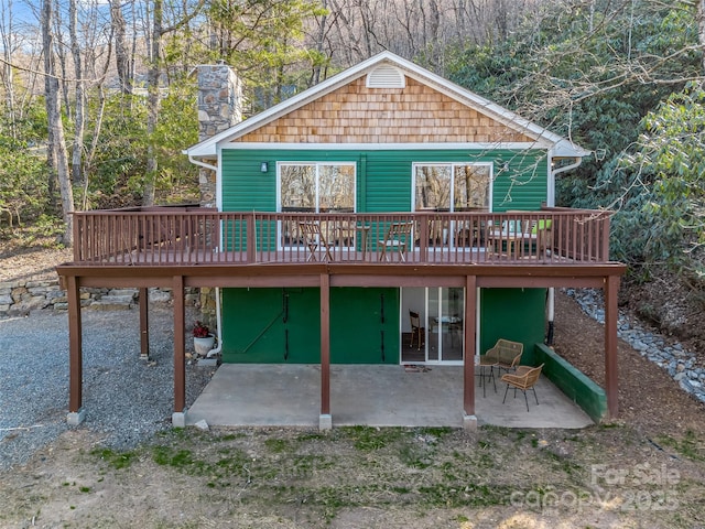 back of house featuring a wooden deck, a chimney, and a patio area