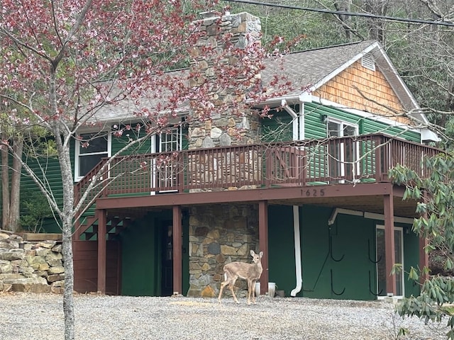 rear view of property with a shingled roof, a wooden deck, and stone siding
