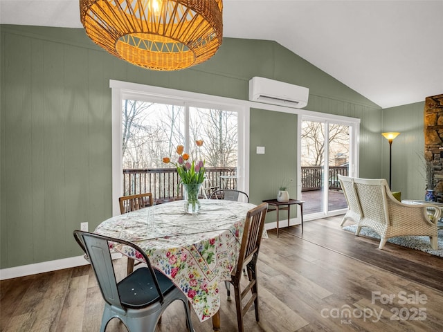 dining room with a wall unit AC, baseboards, vaulted ceiling, and wood finished floors