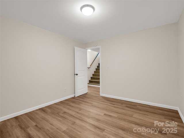 unfurnished room featuring baseboards, light wood-style flooring, and stairs
