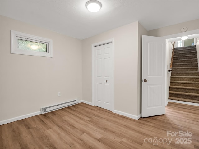 unfurnished bedroom with baseboards, a closet, light wood-style flooring, and a baseboard heating unit