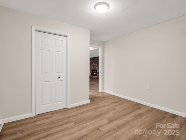 empty room featuring baseboards, a fireplace, and light wood-style flooring