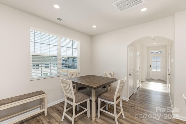 dining space with wood finished floors, arched walkways, and visible vents