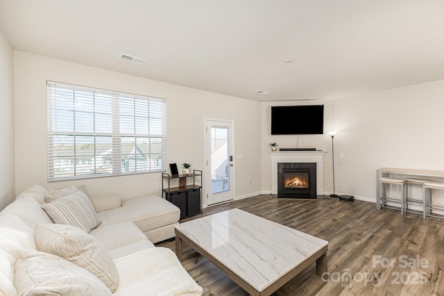 living room featuring baseboards, visible vents, a tiled fireplace, and wood finished floors