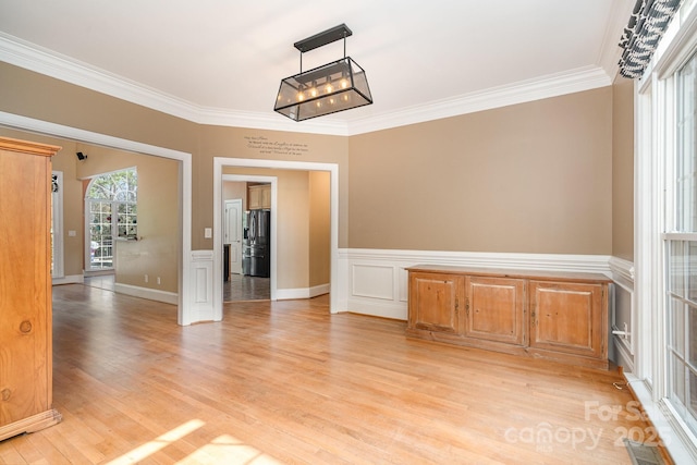 unfurnished dining area with light wood-type flooring, ornamental molding, a wainscoted wall, and visible vents