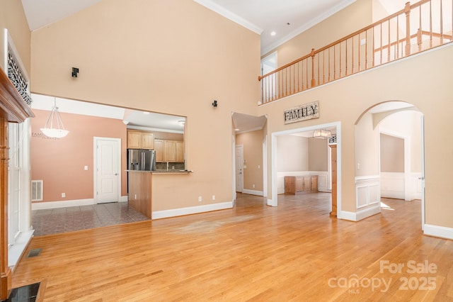 unfurnished living room with crown molding, visible vents, light wood finished floors, and a towering ceiling
